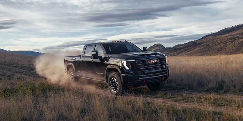 GMC heavy-duty pickup truck driving off-road through a dusty mountain landscape.